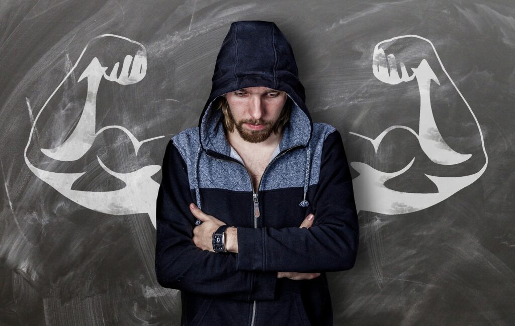 Picture of a hooded man looking down with muscles drown on the wall behind him pondering how to finish the year strong